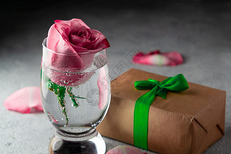 粉红玫瑰在一杯水中 玫瑰花瓣和一盒餐桌上的礼物图片