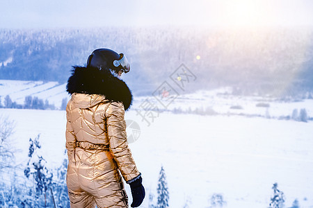 身穿金色滑雪服和头盔的年轻女子站在斜坡顶上 望着距离图片