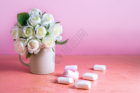 小白色和粉红色棉花糖散布在一朵玫瑰花瓶旁边的浅色粉色背景上 文本位置 假期 问候卡图片