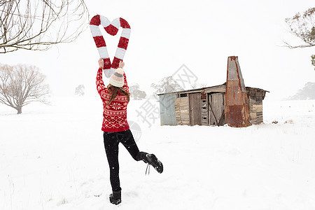 女人拿着圣诞糖果甘蔗 在雪地的风景中以心形形状图片