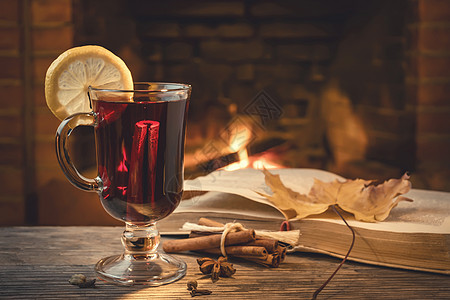 一杯糖红酒 香料 一本在舒适房间桌桌上的书和燃烧的壁炉图片