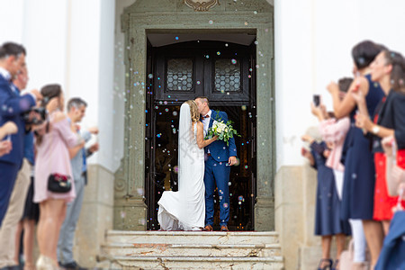 新婚夫妇在婚礼后离开教堂时亲吻 家人和朋友用肥皂泡淋浴庆祝他们的爱 破坏传统米浴的习俗 婚姻 家庭图片