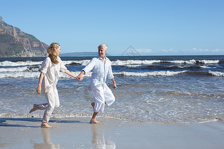 快乐的一对夫妇在海滩上光脚跳过海边图片