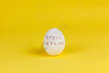 一个白鸡蛋 上面写着复活节快乐 在黄色背景上用邮票和粉红色金属漆写成 复制空间DIY 节日概念 侧面图 水平的图片