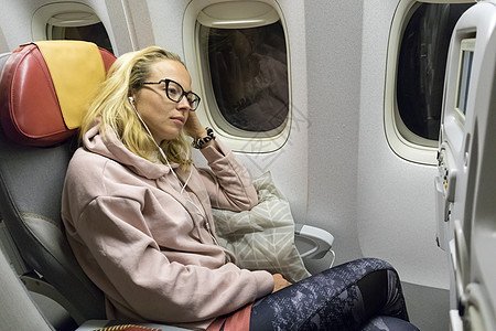 疲倦的金发美女随随便便的caucasian女士在坐着不舒适的座位上睡觉时乘飞机旅行图片
