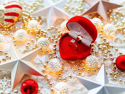 白色针织背景上的圣诞节和新年明星装饰品 带订婚金戒指的红心礼盒 带精致图案的金属灯泡 珠子 柔和的 盒子图片