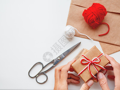 用牛皮纸包裹的 DIY 礼物 礼物用白色和红色的线包装和捆扎 在白色背景上的手中的框 手工制作的 新年图片