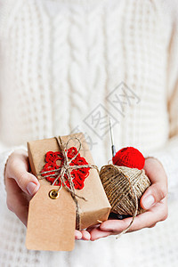 穿着白色针织毛衣的女人手里拿着一份用牛皮纸包装的礼物 上面有红色的钩编雪花 DIY 圣诞节或新年 情人节礼物图片