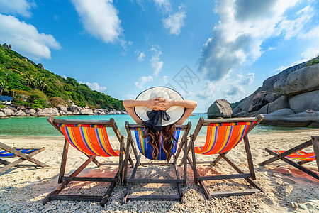 戴着帽子的女人坐在美丽的热带海滩的椅子上 在岛的热带海滩上放松的女人 夏天 躺椅图片