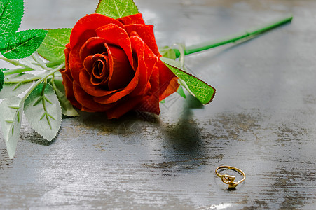 在质朴的金属地板上关闭黄金订婚戒指首饰 柔和的焦点浪漫红色玫瑰花在背景中 情人节婚礼和假期的爱情建议或建议概念 复制空间 结婚戒图片