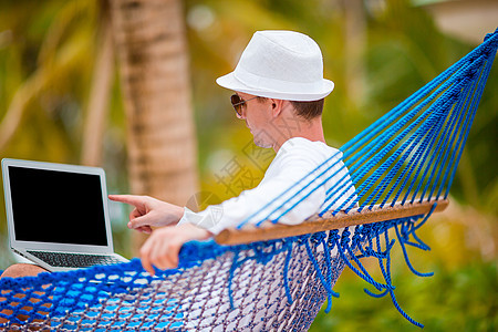 在热带度假的吊床上带笔记本电脑的青年男子 微笑 秋千图片