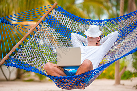 在热带度假的吊床上带笔记本电脑的青年男子 夏天 微笑图片