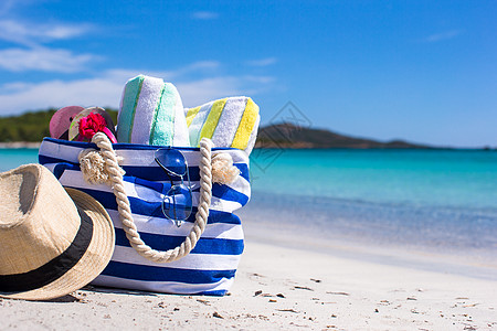 白色热带沙滩上的蓝包 草帽 翻页花圈和毛巾 稻草 绿松石图片