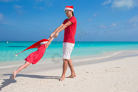 圣诞帽子的小女孩和快乐爸爸 在热带海滩玩得开心 旅行 加勒比图片