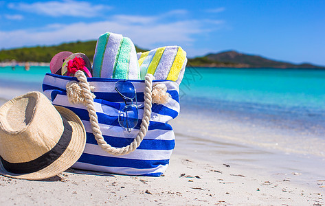 白沙滩上的蓝包 草帽 翻滚式拖鞋和毛巾 海图片