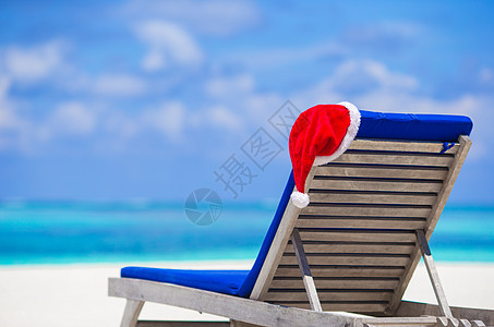 热带白色海滩和绿绿水上带红色圣诞礼帽的太阳椅子休息室 天空 马尔代夫图片