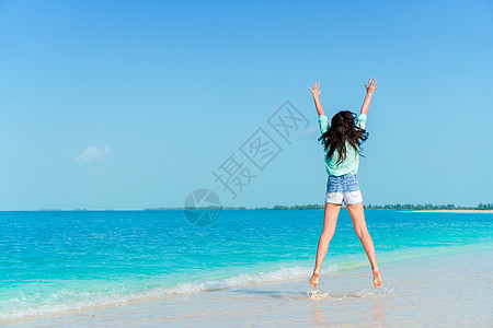 年轻女子在白沙滩上跳跃和举起手臂图片