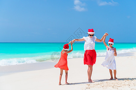 在庆祝圣诞节的热带海滩上 戴红色圣诞老人帽子的美丽家庭快乐 幸福 女儿图片
