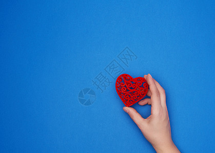女性手握着蓝色背景的红心结在蓝色背景上图片