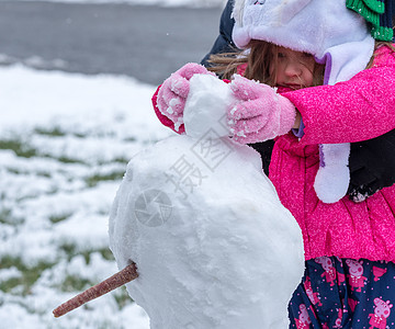 托德勒女孩在前花园的雪里玩 冬天 滚雪球 有趣的背景图片