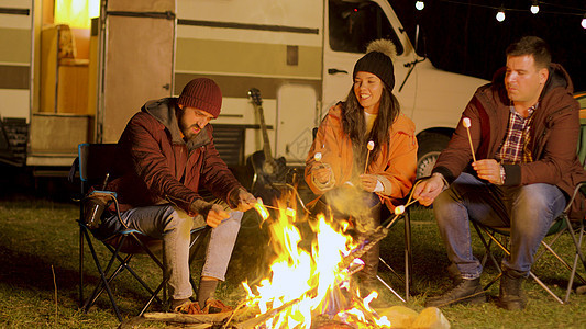 朋友们在露营的火炉周围放松 烧棉花糖棒 团体图片