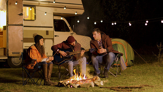 男人在营地火场周围 为朋友唱吉他歌 分享 棉花糖图片