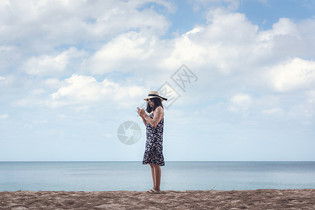 亚洲女性的肖像是在蓝天和沙滩上使用手机 美丽的女人在海滩上度过暑假时正在玩手机 放松的生活方式图片