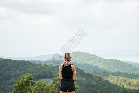 穿着黑色 T 恤的女人的背面 享受热带森林与红树林的景色 蓝天上的群山和白云 热带暑假度假概念 女士 徒步旅行图片