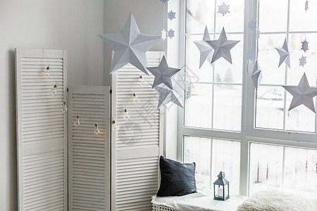 明亮的大窗户 窗台上是灰色针织格子 上面有礼物和闪闪发光的她的土地 纸圣诞星悬挂在窗户的背景上图片