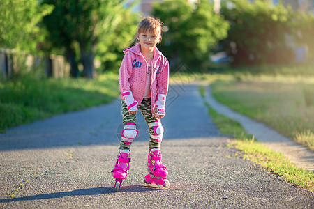 拎着轮滑鞋穿着粉色滚滚机和粉红色毛衣的小女孩在公园里装扮 微笑着笑 学习 体育场背景