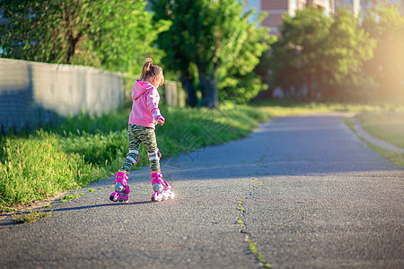 拎着轮滑鞋夏天 一个小女孩在沥青上骑着粉红色溜冰鞋 这孩子学会了骑滑雪鞋 粉色的 学习背景