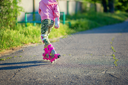 拎着轮滑鞋夏天 一个小女孩在沥青上骑着粉红溜冰滑雪滑冰 没有背面的相片背景
