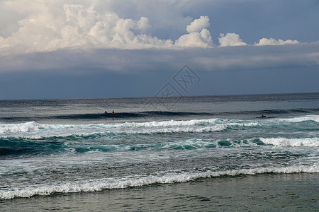 冲浪者正在他们的冲浪板上等待方便的浪潮 巴厘岛上的海滩是热带冲浪者的天堂 湛蓝的天空 阳光灿烂的日子 汹涌的海浪成排地逼近岸边 图片