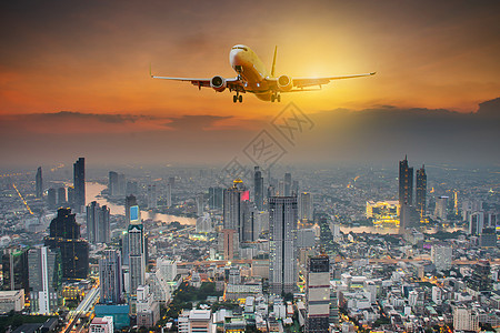 日落时夜城的全景和白色客机 在城市上空空中飞翔的白客机图片
