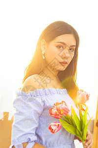 穿着蓝裙子的亚洲美女 带着红色郁金香花 在窗外清晨阳光照在手边图片