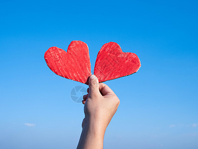 蓝天背景下的手拿着两个红色心形回收纸板 情人节的爱情象征 爱情和浪漫的概念图片
