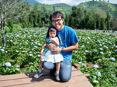 夏日 快乐的父亲和他的女儿坐在木地上 树上有山脉背景 蓝天下 裙子 季节图片