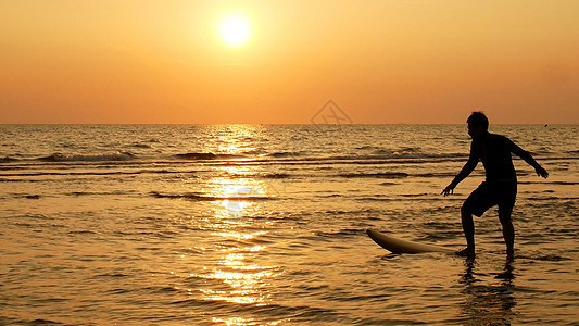 日落时在热带海滩上用长冲浪板冲浪的快乐冲浪人的剪影 海滩上的冲浪者在日落时分与美丽的光线 冲浪水上运动户外活动图片