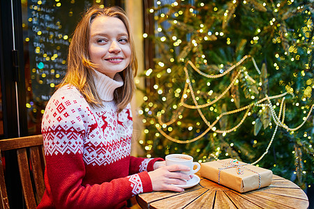穿着假日毛衣的女孩在为圣诞节装饰的咖啡馆里喝咖啡或热巧克力 圣诞老人 温暖的图片