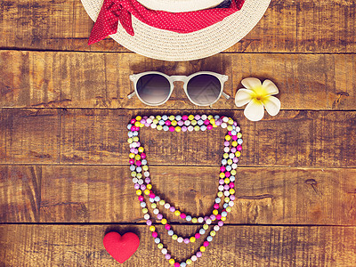 平躺的帽子 项链 太阳镜 花朵和红心形作为旅行者的配饰 在带有复制空间的木制背景下度过暑假 喜欢旅行和度假的女孩 女人图片