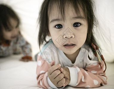 亚洲小女孩的肖像躺在床上的一条白色毯子下 看着相机 可爱的脸孔 与家人的休闲时光图片