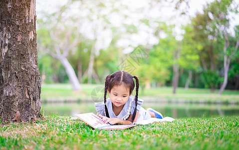 可爱的小女孩在公园里 躺在公园里看书读书图片