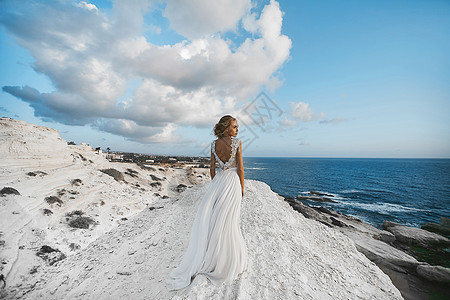 身着白裙子的美丽金发年轻模特女孩 站在白色岩石上 看着大海图片