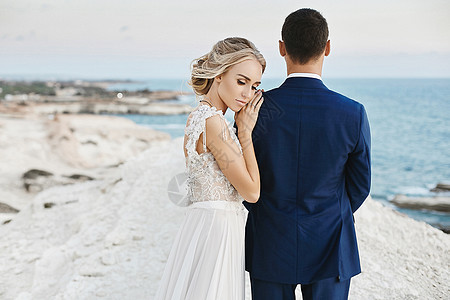 穿着时髦的白色蕾丝裙的漂亮年轻金发女郎靠在穿着时髦蓝色西装的帅哥身上 在亚得里亚海沿岸的白色岩石上摆姿势 裙子 快乐的图片