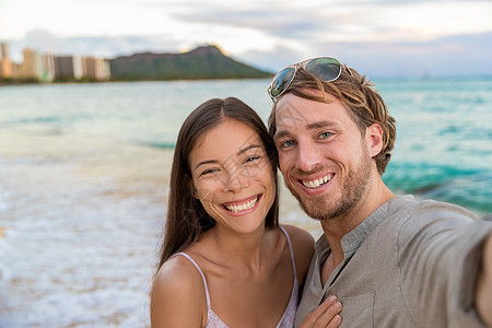 在Waikiki海滩的自已夫妇在夏威夷火奴鲁鲁 Honolulu 海滩上用智能手机拍照 晚上外出散步 旅行目的地 青年人在哈瓦伊图片