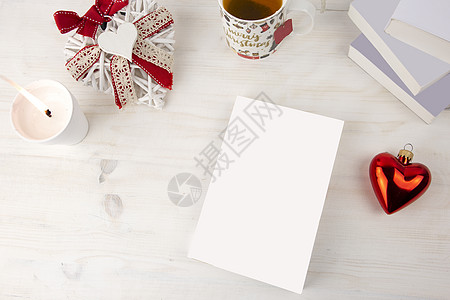 从顶部看一本书的圣诞景色 空白封面的书 上面点着白蜡烛 圣诞装饰的茶杯 红心摆设 浅色木桌上装饰破旧的白心 嘲笑图片