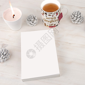 从顶部看书的圣诞背景 空白封面的书 上面点着白蜡烛 圣诞装饰的茶杯 浅色木桌上放着白松果图片