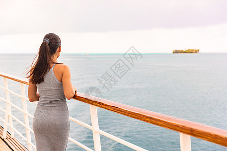 热带海洋旅行的豪华游轮假期-年轻的女游客在游船甲板上看日落 大溪地目的地 背景中的岛屿背景图片