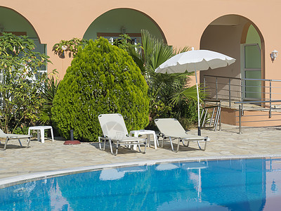 阳光明日 暑假期间空的旅馆游泳池 在希腊科孚岛Corfu岛水池 白防晒床 雨伞和绿棕榈中看到蓝水图片