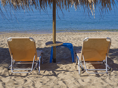 在希腊沙滩上用太阳雨伞 关闭两座黄色空的阳光床 并装有绿绿绿色清蓝海水 米科诺斯岛 地中海图片
